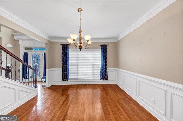 unfurnished dining area with crown molding, wood-type flooring, and a chandelier