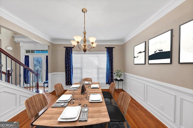 dining space with wood-type flooring, ornamental molding, and a notable chandelier