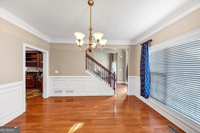 unfurnished dining area with hardwood / wood-style flooring, ornamental molding, and a chandelier