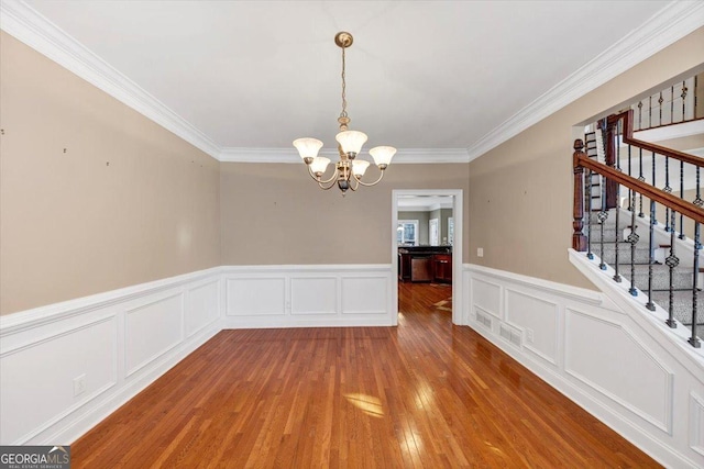 unfurnished dining area featuring ornamental molding, hardwood / wood-style floors, and a notable chandelier