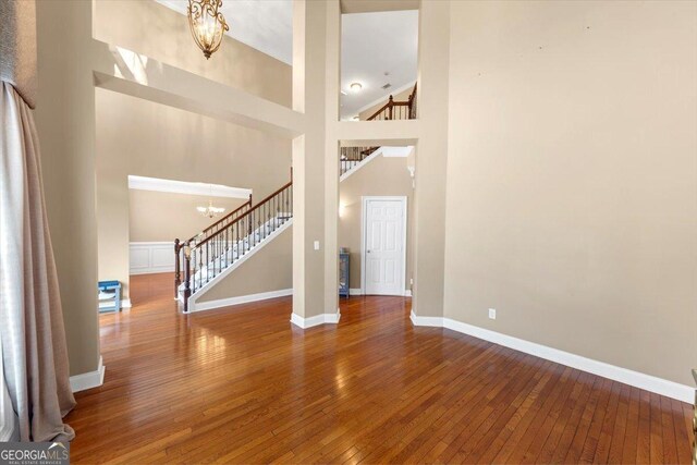 unfurnished living room with hardwood / wood-style floors, a chandelier, and a high ceiling