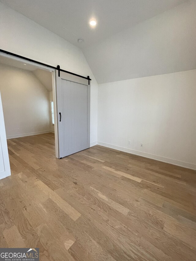 bonus room featuring light wood-type flooring, a barn door, and vaulted ceiling