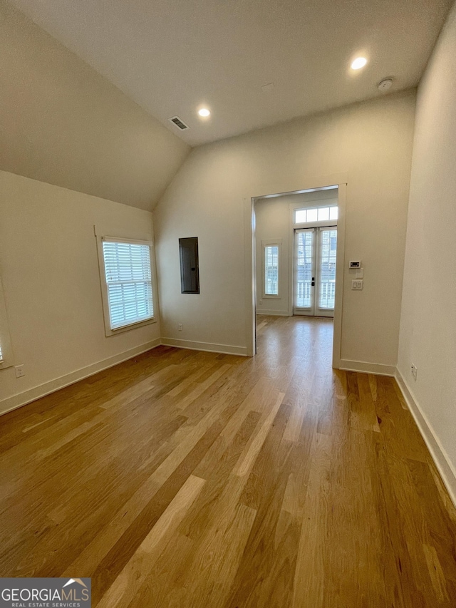 unfurnished living room with light wood-type flooring, lofted ceiling, and french doors