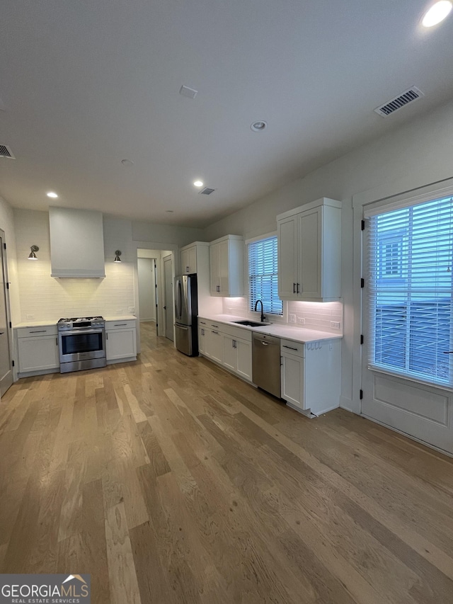 kitchen featuring sink, stainless steel appliances, backsplash, light hardwood / wood-style floors, and white cabinets