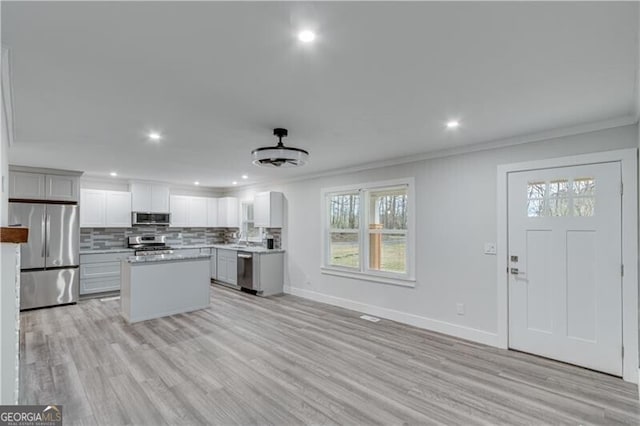 kitchen with stainless steel appliances, tasteful backsplash, light hardwood / wood-style flooring, a kitchen island, and ornamental molding