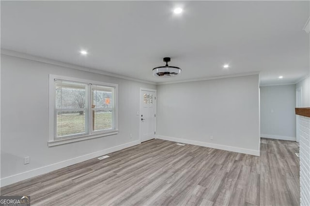 empty room featuring a brick fireplace, light hardwood / wood-style flooring, and ornamental molding