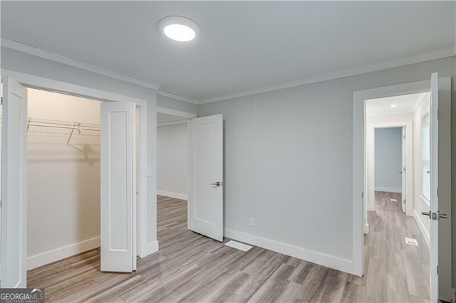 unfurnished bedroom featuring a spacious closet, a closet, light hardwood / wood-style floors, and ornamental molding