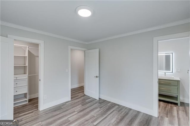 unfurnished bedroom featuring a spacious closet, a closet, light hardwood / wood-style flooring, and ornamental molding