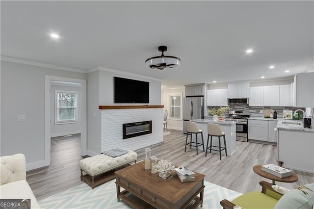 living room featuring light hardwood / wood-style floors, ornamental molding, sink, and a brick fireplace