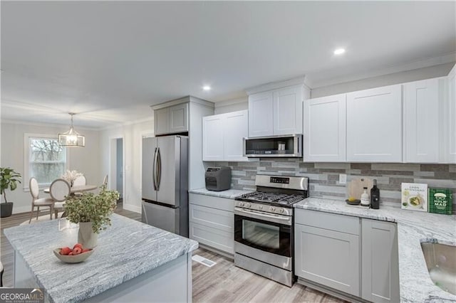 kitchen with pendant lighting, decorative backsplash, light stone countertops, ornamental molding, and stainless steel appliances