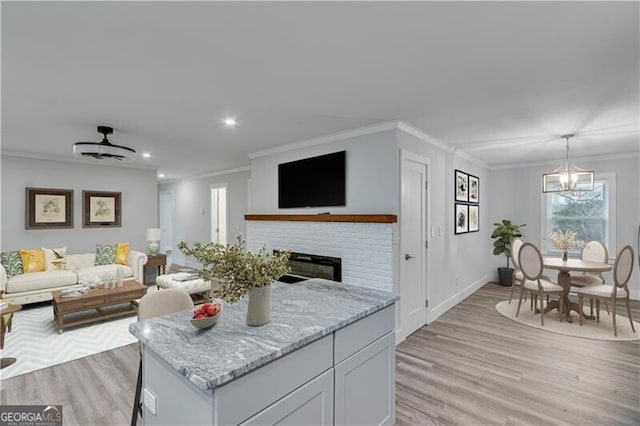 living room with light wood-type flooring, a brick fireplace, crown molding, and a notable chandelier