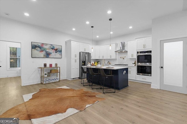 kitchen featuring pendant lighting, wall chimney range hood, an island with sink, a kitchen bar, and stainless steel appliances