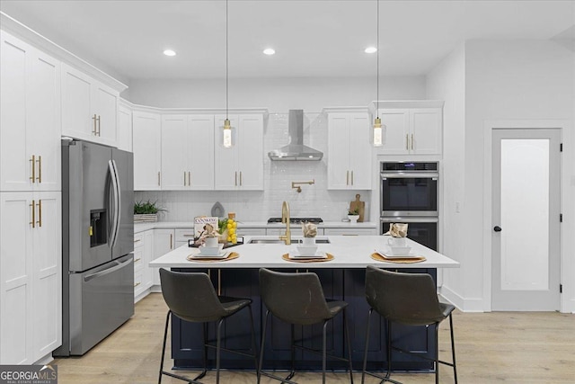 kitchen featuring pendant lighting, wall chimney exhaust hood, white cabinetry, and appliances with stainless steel finishes