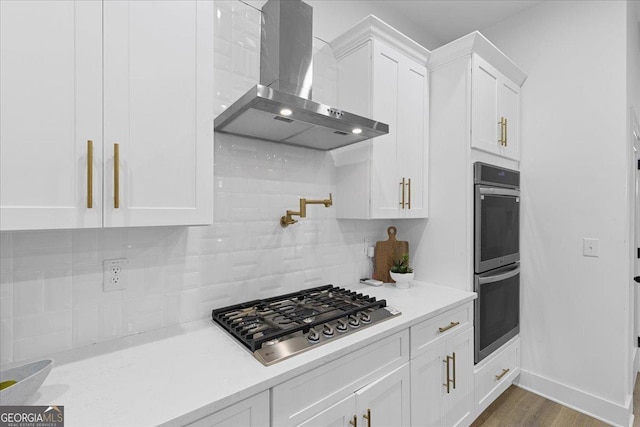 kitchen featuring dark wood-type flooring, white cabinets, wall chimney exhaust hood, decorative backsplash, and stainless steel appliances