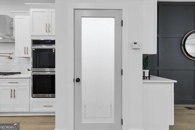 kitchen with decorative backsplash, gas cooktop, stainless steel double oven, light hardwood / wood-style flooring, and white cabinets