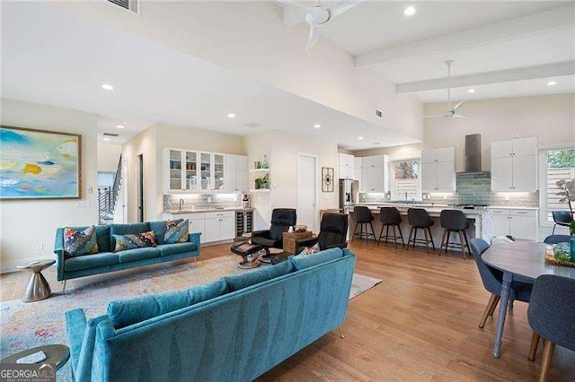 living room with beamed ceiling, light wood-type flooring, ceiling fan, and sink