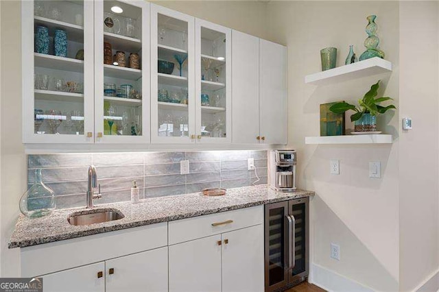 bar featuring sink, decorative backsplash, light stone countertops, white cabinetry, and beverage cooler