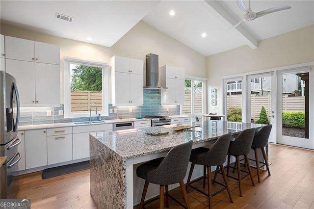 kitchen featuring white cabinetry, a center island with sink, wall chimney range hood, and sink