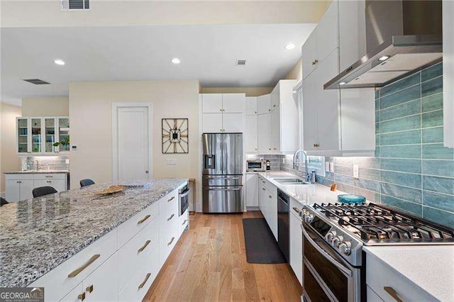 kitchen featuring white cabinetry, sink, wall chimney range hood, light hardwood / wood-style floors, and appliances with stainless steel finishes