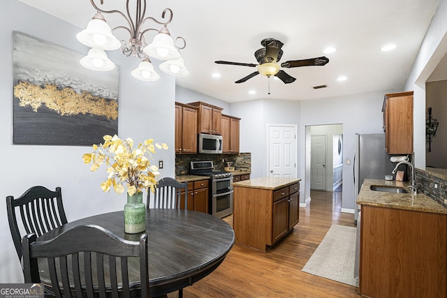 kitchen featuring sink, hanging light fixtures, stainless steel appliances, ceiling fan with notable chandelier, and light wood-type flooring