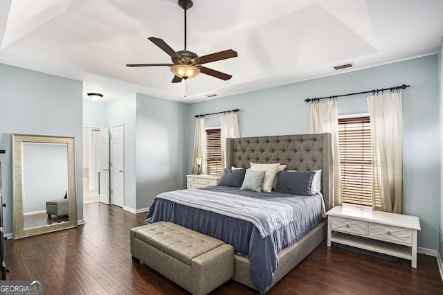 bedroom with a tray ceiling, dark hardwood / wood-style floors, and ceiling fan