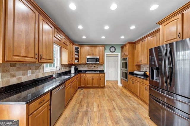 kitchen featuring decorative backsplash, light wood-type flooring, stainless steel appliances, sink, and dark stone countertops