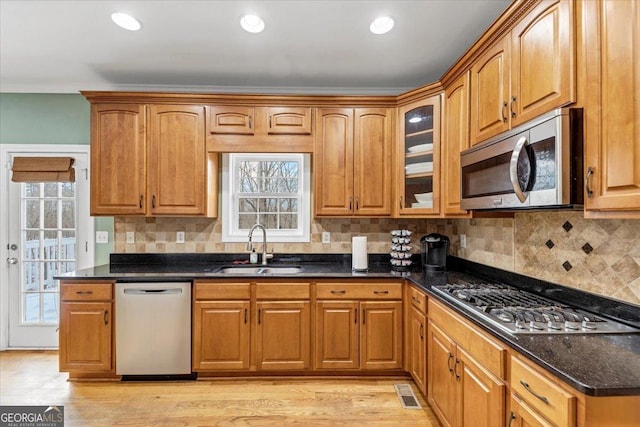 kitchen featuring backsplash, dark stone counters, sink, light hardwood / wood-style flooring, and stainless steel appliances