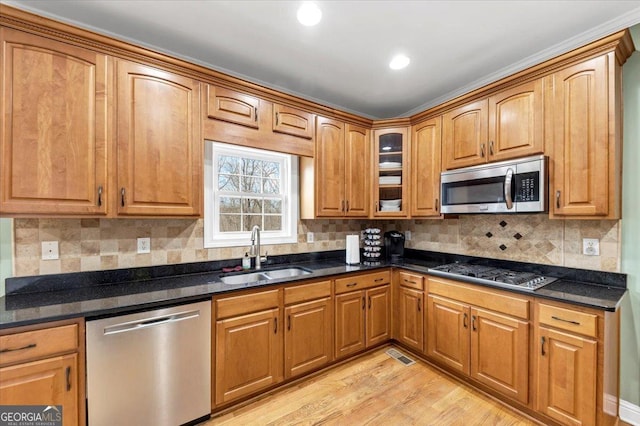 kitchen with appliances with stainless steel finishes, light wood-type flooring, tasteful backsplash, dark stone counters, and sink