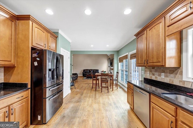 kitchen with backsplash, dark stone countertops, ornamental molding, light hardwood / wood-style floors, and stainless steel appliances