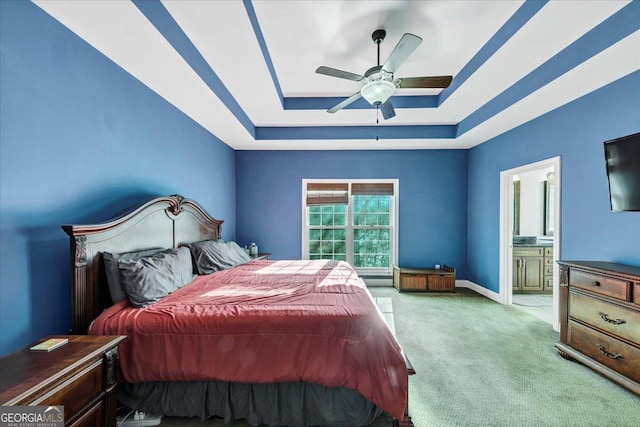 carpeted bedroom featuring ensuite bathroom, ceiling fan, and a tray ceiling