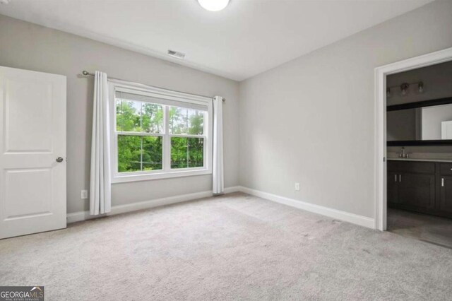 unfurnished bedroom with connected bathroom and light colored carpet