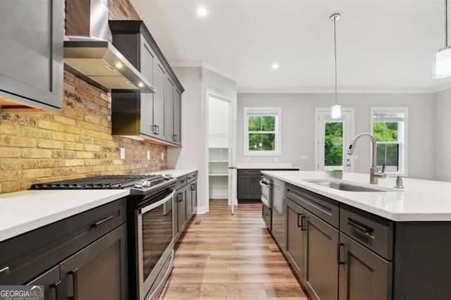 kitchen featuring a healthy amount of sunlight, light countertops, appliances with stainless steel finishes, wall chimney exhaust hood, and a sink