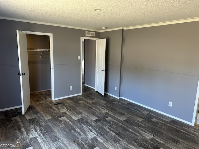 unfurnished bedroom featuring a textured ceiling, a spacious closet, a closet, and dark wood-type flooring