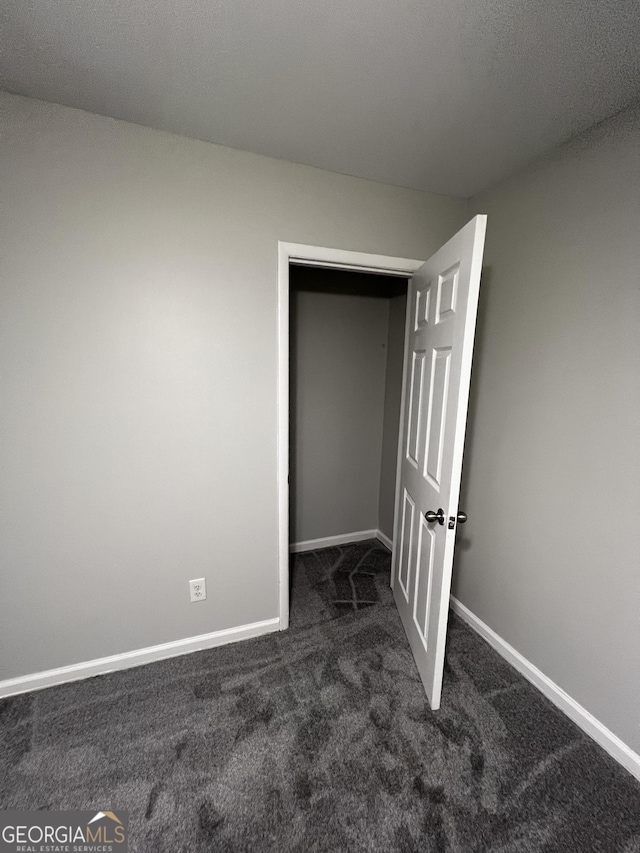 unfurnished bedroom featuring dark carpet and a closet