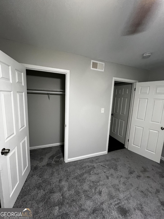 unfurnished bedroom with a closet, a textured ceiling, and dark colored carpet