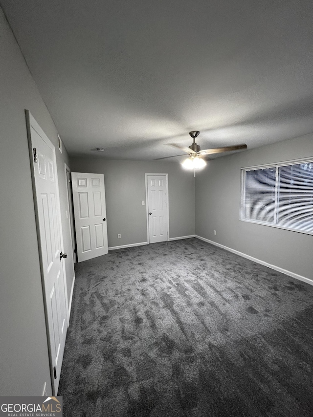 unfurnished bedroom with ceiling fan, a textured ceiling, and dark colored carpet