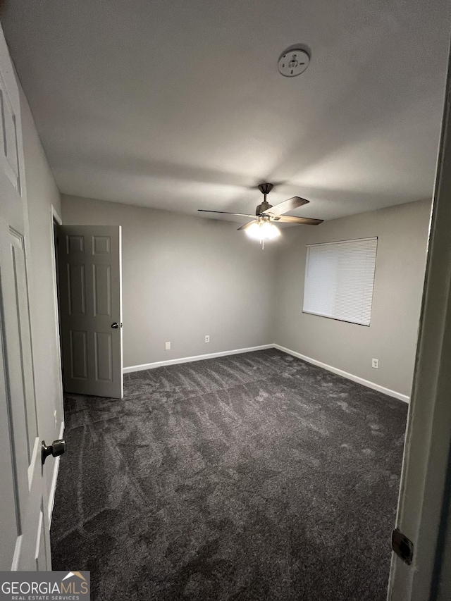 empty room featuring ceiling fan and dark carpet