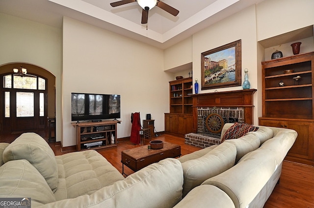 living room featuring dark hardwood / wood-style flooring, a brick fireplace, ceiling fan, and a high ceiling