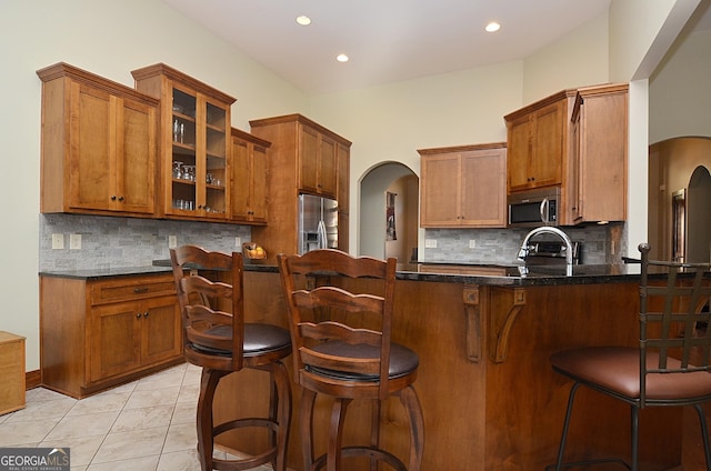 kitchen with appliances with stainless steel finishes, kitchen peninsula, dark stone counters, and decorative backsplash