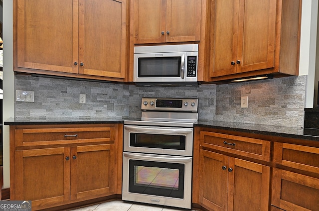 kitchen featuring tasteful backsplash, light tile patterned floors, dark stone counters, and appliances with stainless steel finishes