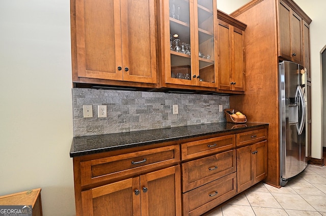 kitchen with light tile patterned floors, stainless steel fridge with ice dispenser, decorative backsplash, and dark stone countertops