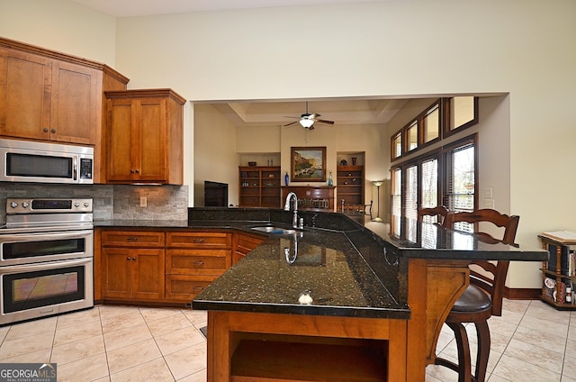 kitchen featuring sink, a kitchen bar, dark stone counters, decorative backsplash, and stainless steel appliances