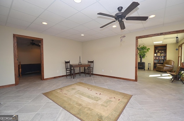 sitting room with a paneled ceiling, ceiling fan, and a wood stove