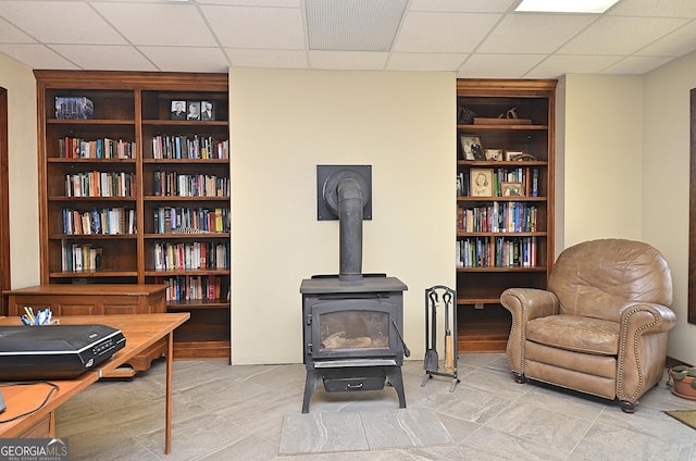 living area with a drop ceiling, built in features, and a wood stove