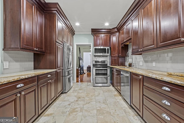 kitchen with appliances with stainless steel finishes, sink, backsplash, ceiling fan, and light stone countertops