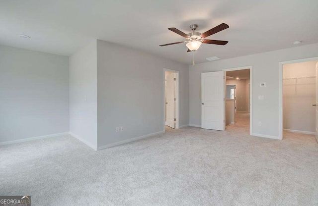 unfurnished bedroom featuring ceiling fan, a walk in closet, light carpet, and a closet