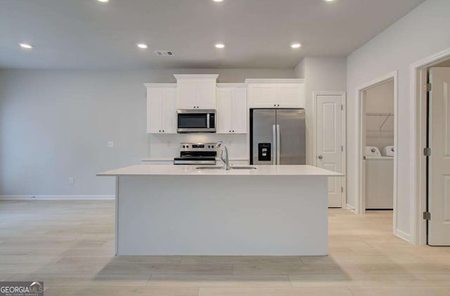 kitchen with a center island with sink, sink, white cabinetry, stainless steel appliances, and washing machine and clothes dryer