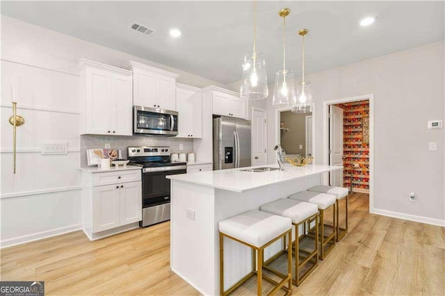 kitchen with pendant lighting, a center island with sink, sink, white cabinetry, and stainless steel appliances