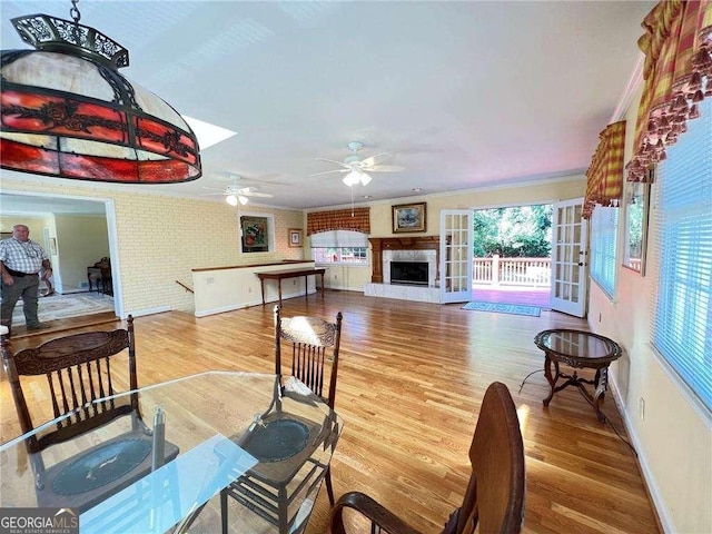 living room with ceiling fan, brick wall, crown molding, hardwood / wood-style floors, and a tiled fireplace