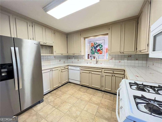 kitchen with sink, backsplash, tile countertops, white appliances, and cream cabinetry